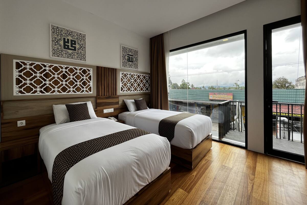 Quarto de hotel com duas camas, cabeceiras de madeira, painéis decorativos na parede e uma janela grande com vista para o exterior.