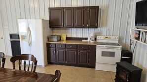 A compact kitchen with dark brown cabinets, a white refrigerator, a stove, and a small black wood stove.