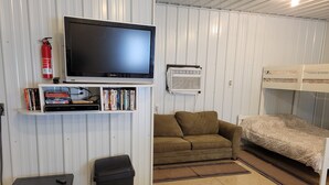 A compact room with a television, a bookshelf, a sofa, a bunk bed, a fireplace, and a fire extinguisher.