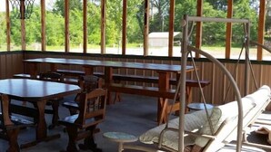 A covered outdoor seating area with wooden tables and benches, surrounded by a wooden fence with vertical slats.
