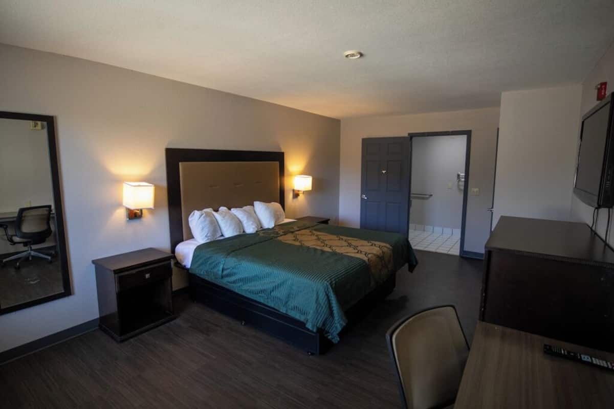 A hotel room with a bed, bedside lamps, a desk, a chair, and a mirror.