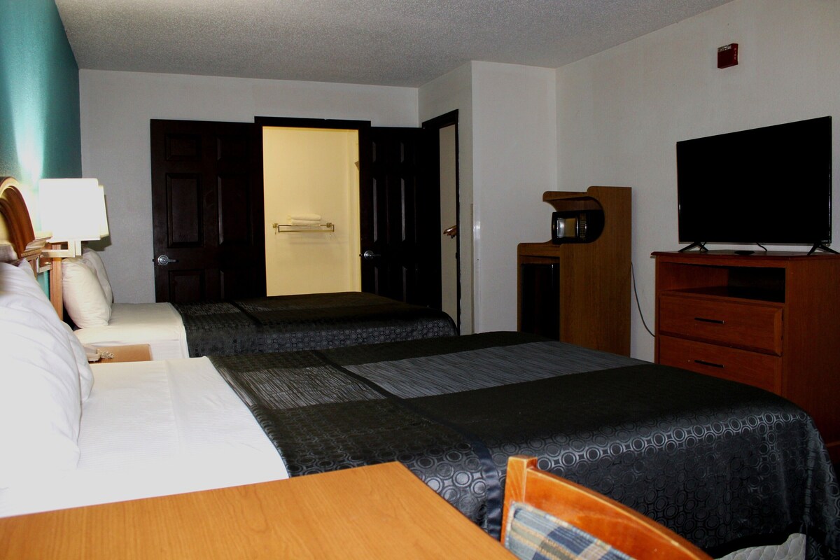 A hotel room with two beds, a TV, a desk, and a door leading to another room.