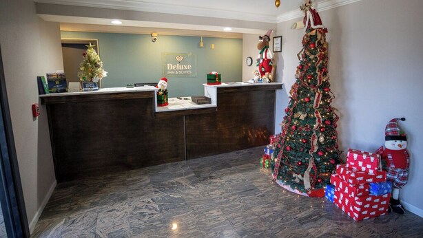 Uma área de recepção de hotel com árvore de Natal, decoração de boneco de neve e um letreiro com a inscrição 'Deluxe Inn & Suites'.