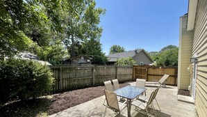 Ein Garten mit Terrasse, Tisch und Stühlen, umgeben von einem Holzzaun und Bäumen.