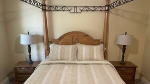 Ein Bett mit Baldachin, ein hölzernes Kopfende, zwei Nachttische mit Lampen und eine gestreifte Bettdecke.