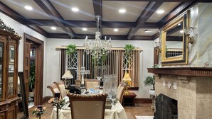 Un comedor con candelabro, sillas de madera, una mesa preparada para cuatro comensales, chimenea y un espejo grande.