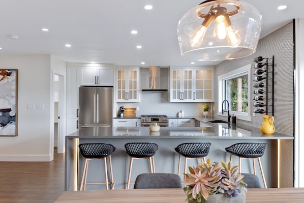 A modern kitchen with stainless steel appliances, a central island with bar stools, and a wine rack by the window. - *Luxury Waterfront* beautiful and peaceful retreat (Port Moody)