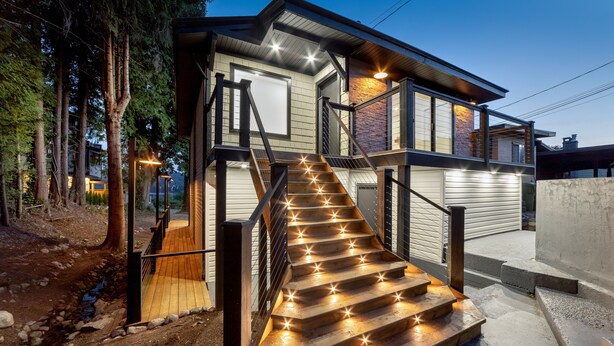 Ein modernes Haus mit einer Holztreppe, die zu einer Terrasse führt, umgeben von Bäumen.
