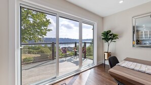 Ein Zimmer mit einer großen Schiebeglasdoor, die auf eine Terrasse mit Blick auf einen See und Bäume führt.