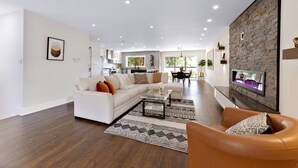 Ein modernes Wohnzimmer mit einem weißen Sofa, einem Ledersessel und einem Couchtisch. Im Hintergrund befindet sich ein Kamin mit einer Steinwand.