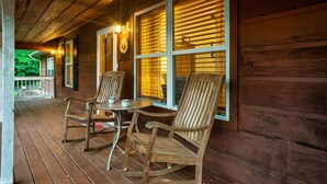 A wooden porch with rocking chairs and a table, featuring large windows with blinds. - Charming Cozy Cabin by the Smoky Mtns. Game Room, Fireplace, Sunroom, Fire Pit (Sevierville)