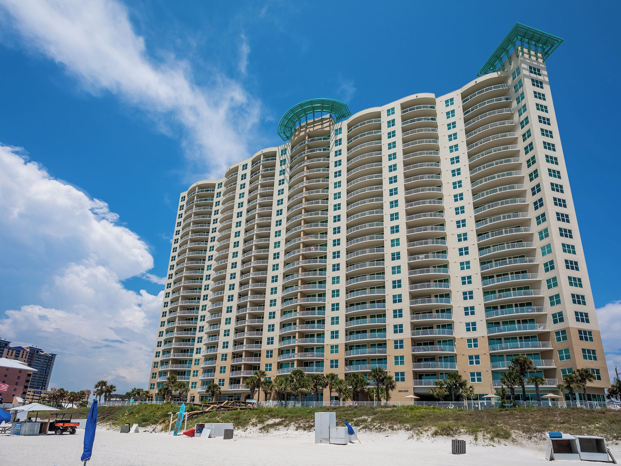 Un hotel moderno de gran altura con varios balcones, vistas a la playa y una estructura distintiva en la azotea.