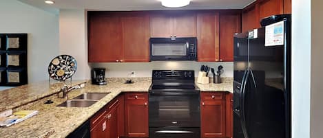A kitchen with granite countertops, wooden cabinets, a black microwave, a black stove, and a black refrigerator.