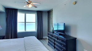 Habitación de hotel con cama, televisor en una cómoda, ventilador de techo y ventana con cortinas.