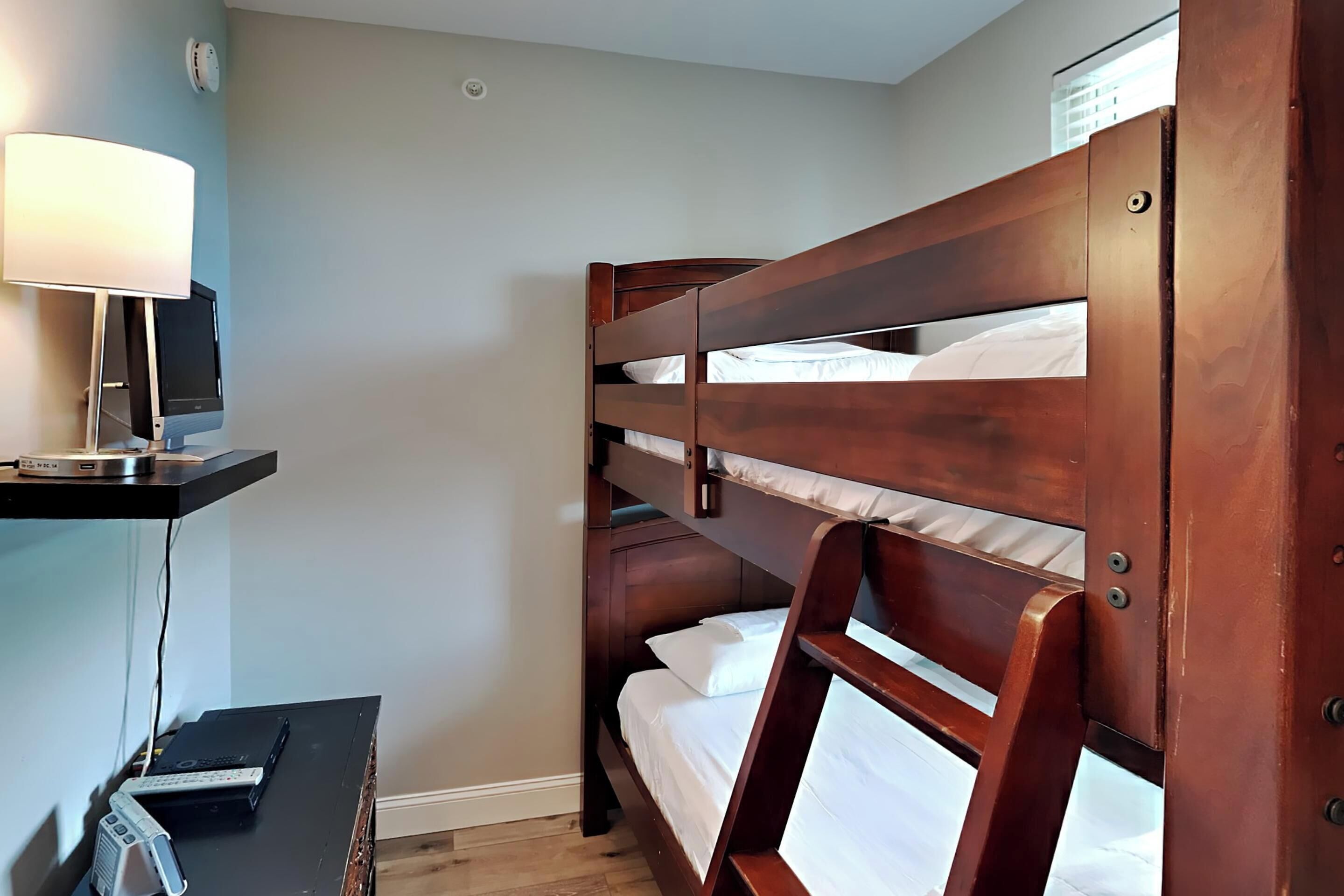 A bunk bed room with a desk and lamp.