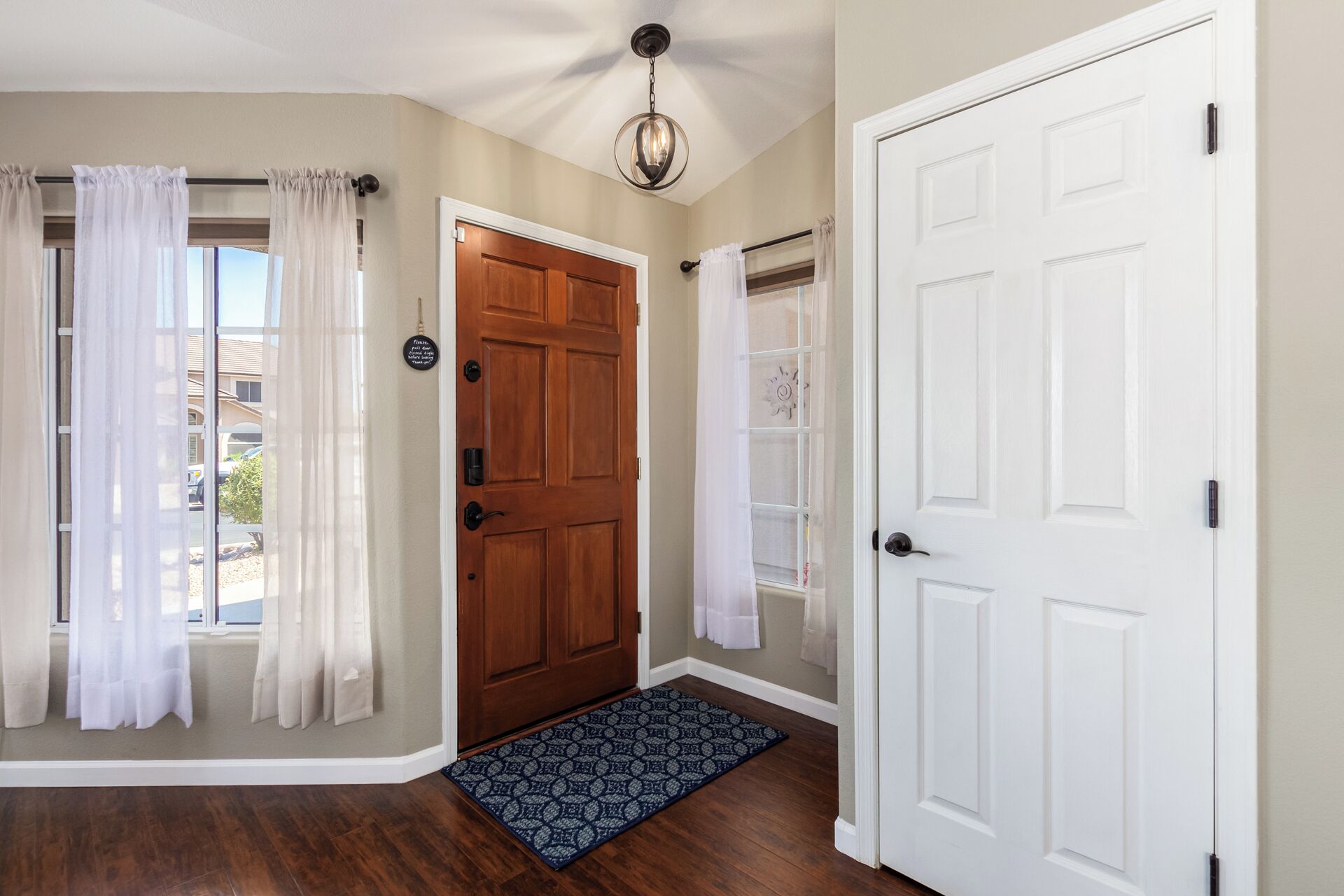 A hallway with a wooden door, a white door, and a glass door with a window. There is a blue patterned rug on the floor.