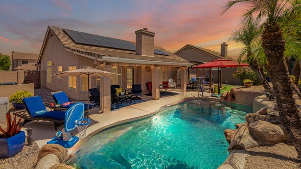 A swimming pool with lounge chairs and umbrellas, a covered patio area, and a house with solar panels. - Resort Style Home, Private"Heated Pool", Near Phoenix.Putting Green, Pool Table. (Mesa)