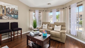A living room with a beige sofa, two black chairs, a wooden coffee table, and a painting of a cityscape. - Resort Style Home, Private"Heated Pool", Near Phoenix.Putting Green, Pool Table. (Mesa)