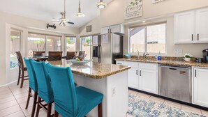 A modern kitchen with white cabinets, a granite countertop, and a central island with teal chairs. - Resort Style Home, Private"Heated Pool", Near Phoenix.Putting Green, Pool Table. (Mesa)