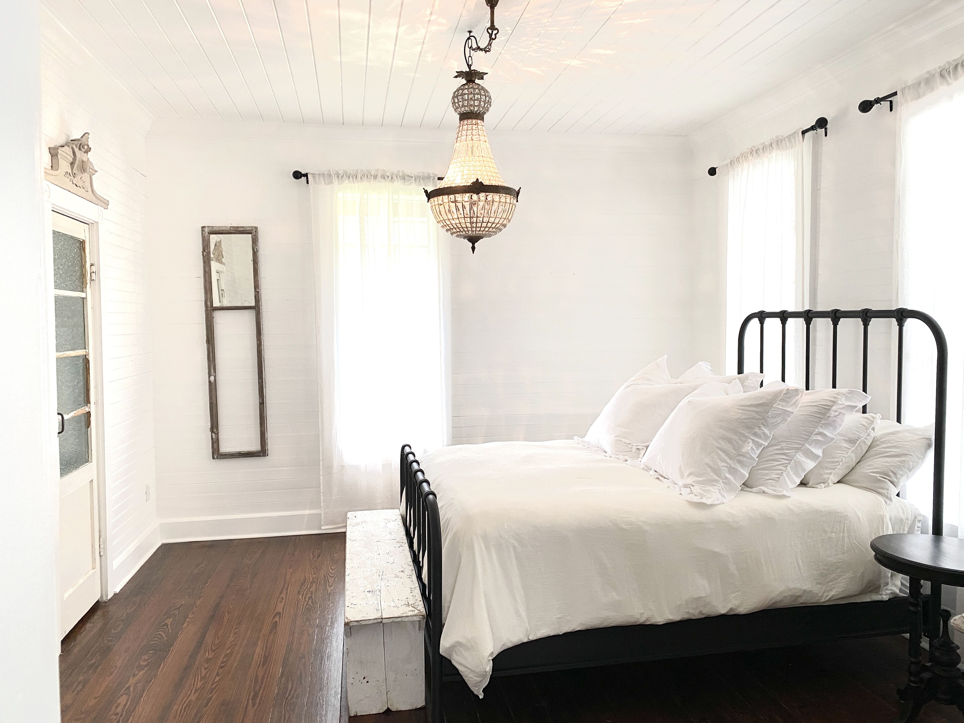 Een slaapkamer met een bed, een kroonluchter, een raam en een deur.