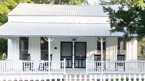 Une maison blanche de style colonial, dotée d’un porche, de deux portes et d’une clôture en piquets.