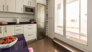 Una cocina moderna con armarios blancos, un refrigerador de acero inoxidable, un microondas y un ventanal con vistas a una terraza de madera.