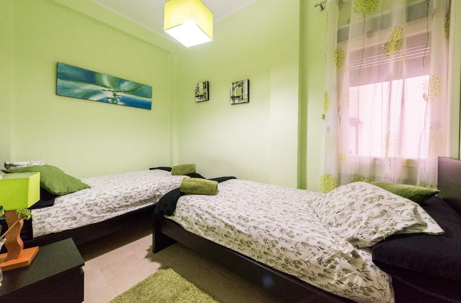 Een kamer met twee eenpersoonsbedden, een tafeltje met een lamp en een schilderij aan de muur.