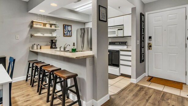 Una cocina moderna con barra, taburetes, refrigerador, microondas y un letrero de bienvenida.