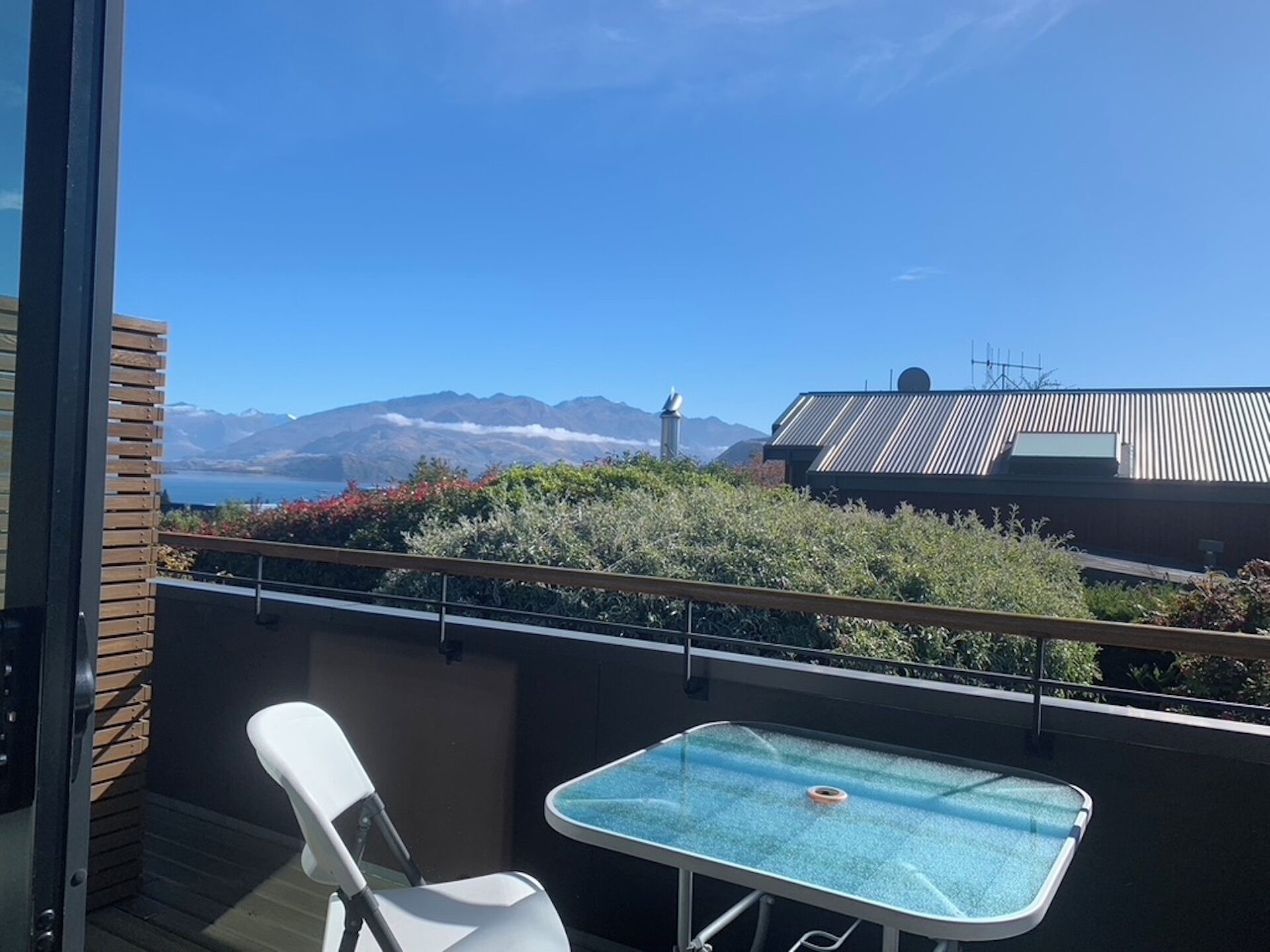 A balcony with a view of mountains, a table, and a chair.