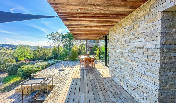 A wooden deck with a table and chairs, a stone wall, and a view of the surrounding landscape.