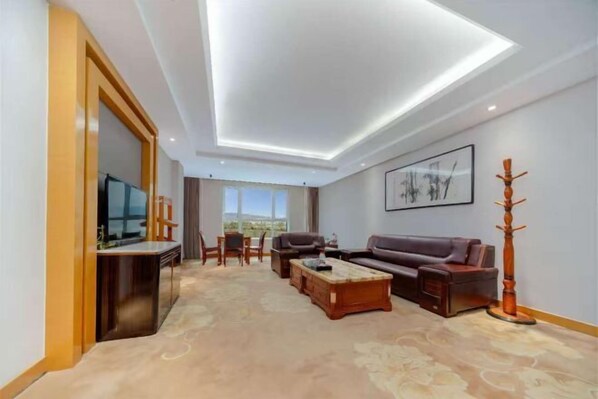 A modern living room with a flat-screen TV, a sofa, a coffee table, and a dining area with chairs.