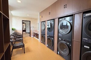 Un lavadero con varias lavadoras, armarios de madera y una zona de estar con sillas.