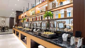 A buffet area with multiple food dispensers, a seating area with tables and chairs, and a decorative shelf with plants and jars.