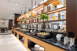 Un espace buffet doté de plusieurs distributeurs de nourriture, un coin repas avec des tables et des chaises, et une étagère décorative agrémentée de plantes et de bocaux.