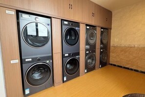 Une buanderie équipée de quatre machines à laver à chargement frontal et de meubles de rangement en bois.