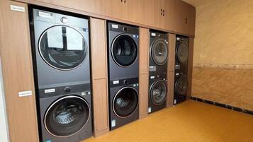 A row of four front-loading washing machines in a laundry room with wooden cabinets above.