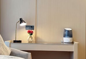 Quarto de hotel com mesa de cabeceira, luminária, um vaso com flores e cafeteira.