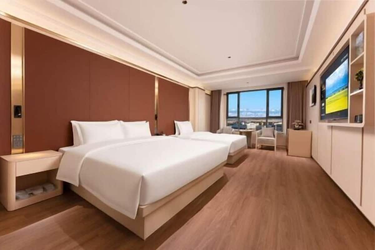 Ein Hotelzimmer mit einem großen Bett, Nachttischen, einem Schreibtisch und Blick auf die Stadt.