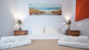 A bedroom with a bed, two nightstands, a painting of a beach scene, and a window with a blind. - Posadilla Apartment Cádiz (Cádiz)