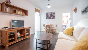 A living room with a TV, wooden entertainment unit, dining table, and sofa. - Posadilla Apartment Cádiz (Cádiz)