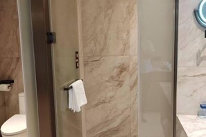 Un baño moderno con cabina de ducha de vidrio, paredes de mármol y un inodoro blanco.