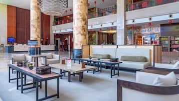 A spacious lobby with multiple seating areas, including sofas and tables, and a large digital screen.