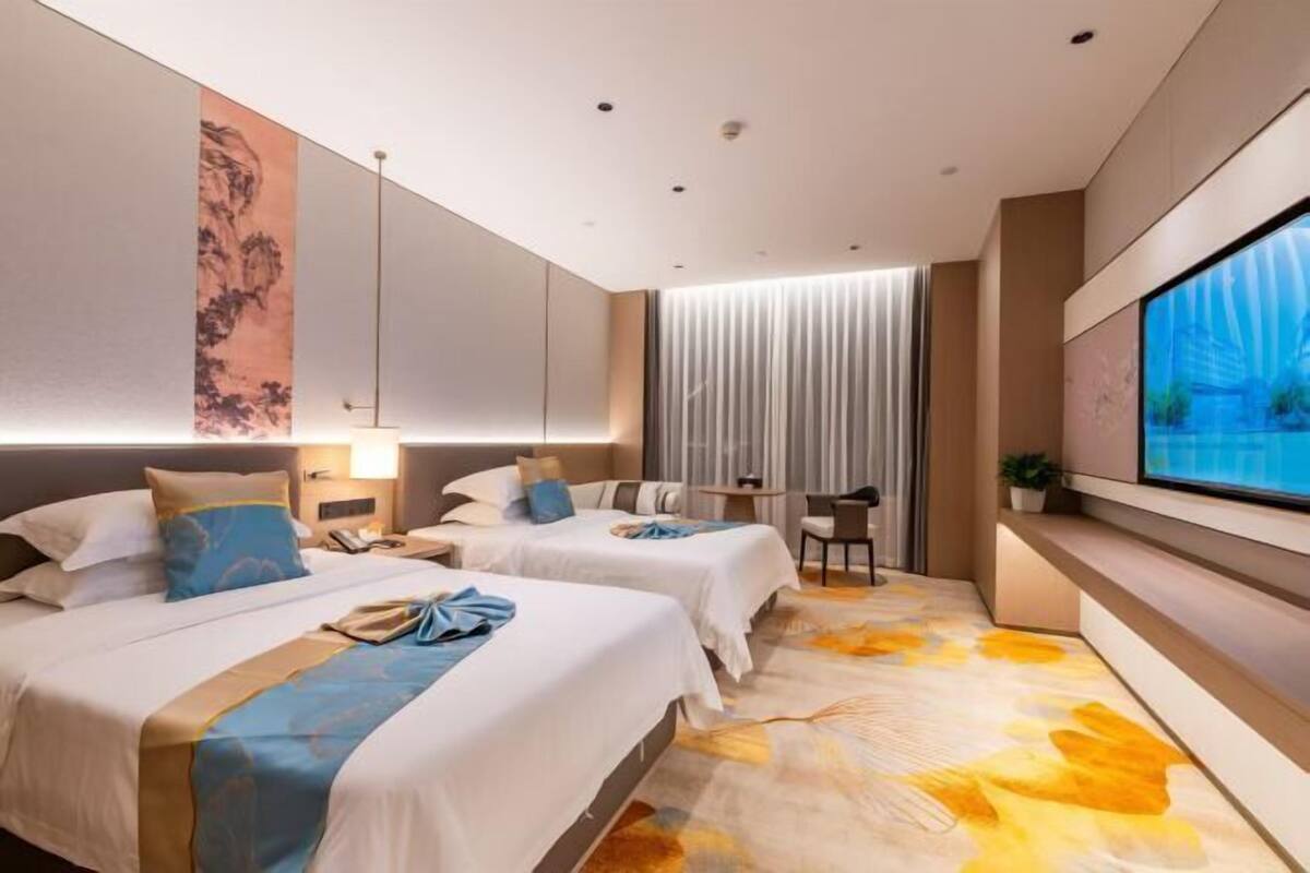 Habitación de hotel con dos camas, un escritorio, un televisor y un ventanal grande.