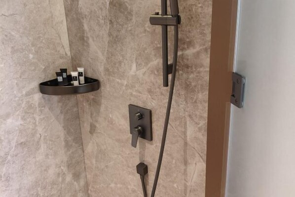 A shower with a handheld showerhead, a wall-mounted control panel, and a shelf with toiletries.