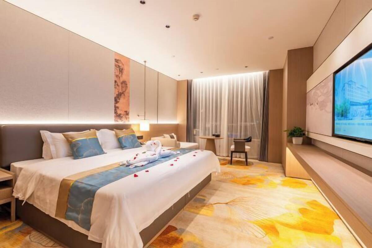 Una habitación de hotel moderna con una cama grande, un escritorio, una silla, un televisor y un ventanal con cortinas.