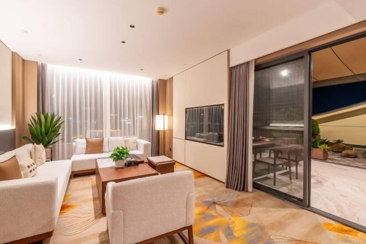 Una habitación de hotel moderna con un conjunto de sofás, una mesa de comedor y un amplio ventanal corredero que da a un espacio exterior.