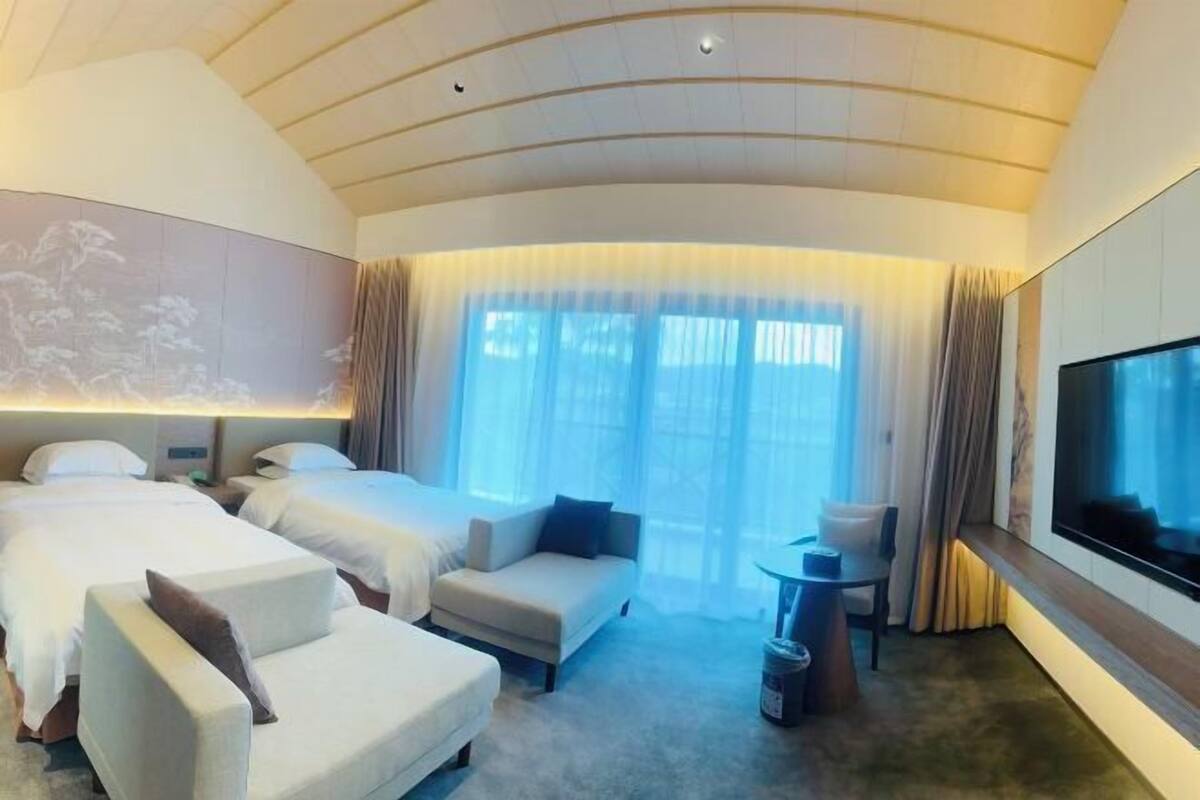 Una habitación de hotel con dos camas, un sofá, una televisión y un ventanal con cortinas.