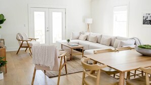 Un intérieur lumineux et blanc, avec un canapé, des fauteuils, une table à manger et une lampe.
