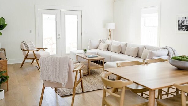 Ein heller, weißer Innenraum mit einer Couch, Sesseln, einem Esstisch und einer Lampe.