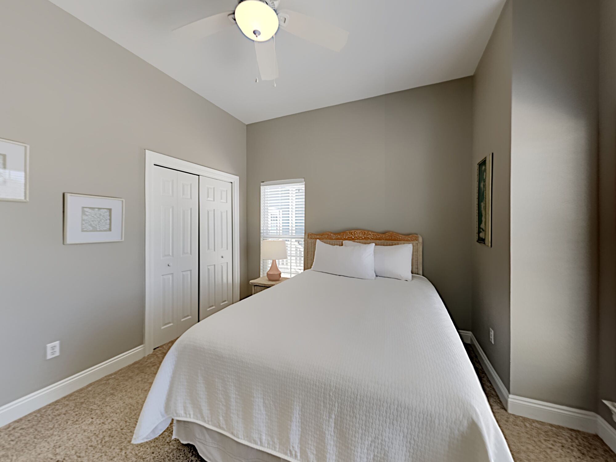 A bedroom with a large bed, a ceiling fan, a nightstand, and a window with blinds.